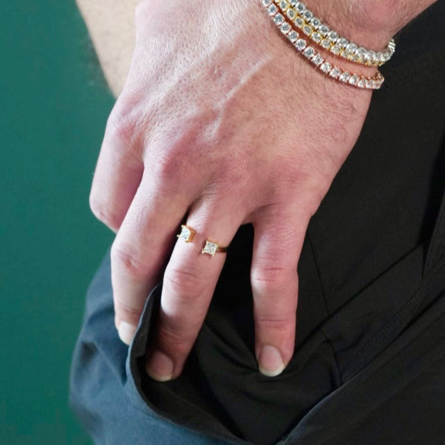 Close-up of a person's hand wearing a ring and bracelets on a green background
